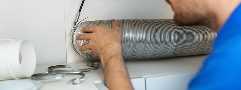Engineer installing flexible aluminum ventilation ducting for kitchen cooker hood. 